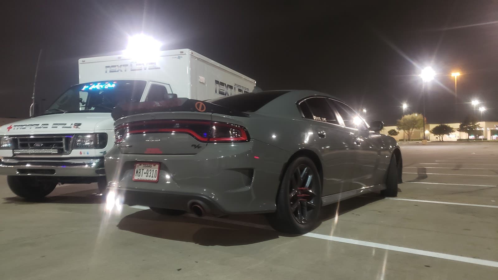 The NXT_L3VL ambulance-wrapped mobile mechanic rig next to a performance Charger at night